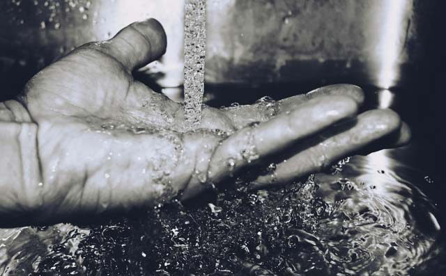 Foto em preto e branco de corrente de água caindo sobre uma mão aberta espalmada.